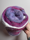 Hand holding a ball of purple and white yarn against a plain background